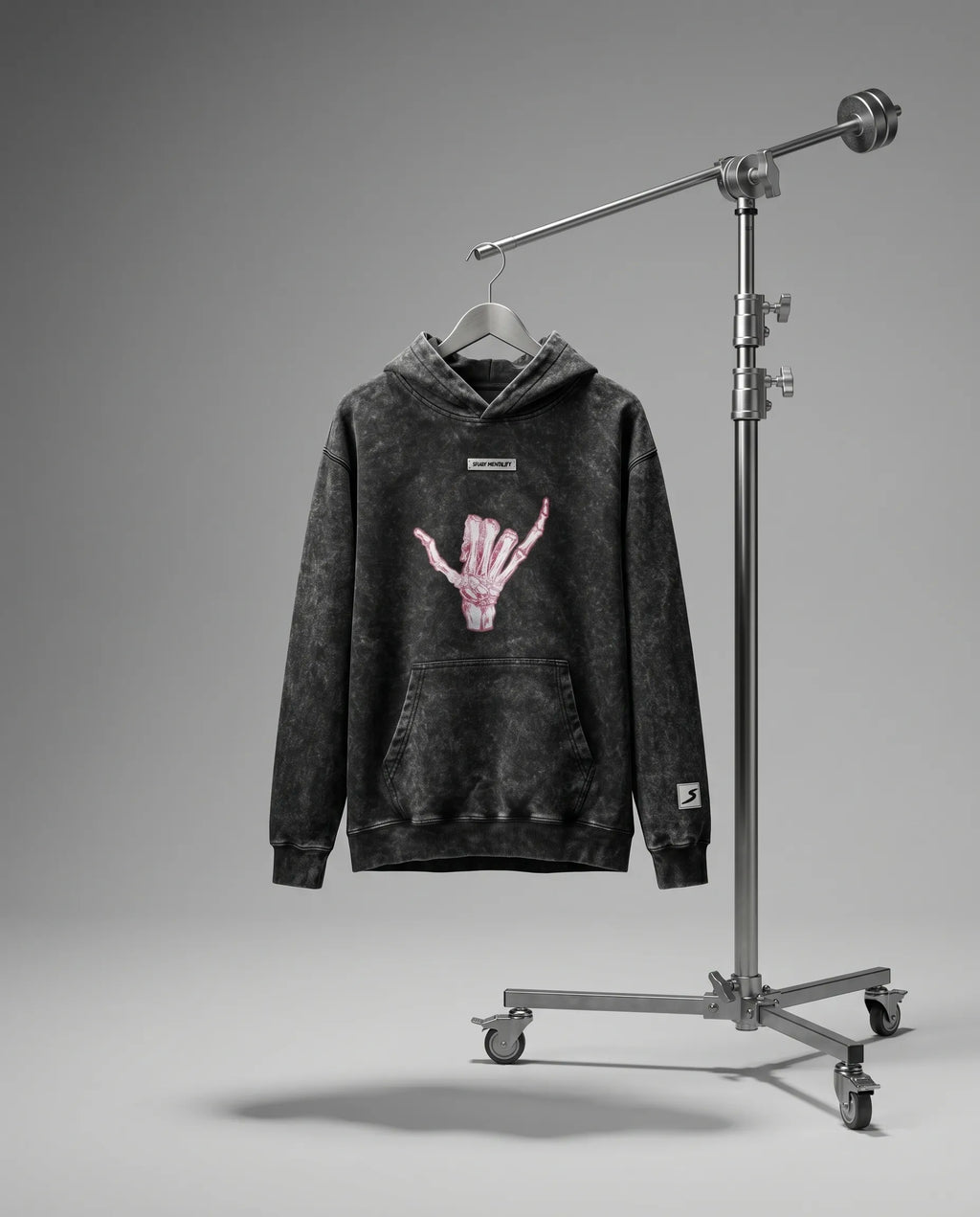 Black hoodie with pink graphic on a hanger next to a studio light stand against a gray background