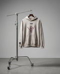 Beige hoodie with a graphic design on a stand against a gray background